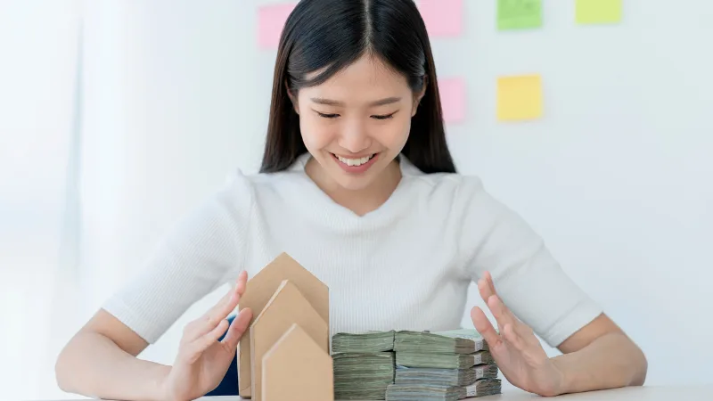 Người phụ nữ cạnh mô hình nhà và xấp tiền