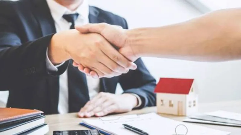 Nhân viên ngân hàng và khách hàng bắt tay bên mô hình ngôi nhà